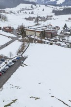 Snow-covered village with parking space in the midst of a winter landscape seen from the air,