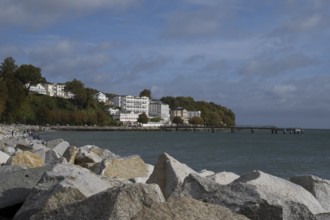Large stones on the shore, behind Hotel Fürstenhof and pier, blue sky and clouds, Sassnitz, Rügen,