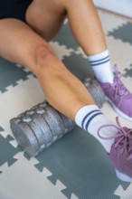 Person performing self massage with a foam roller on the calf muscle, engaging in sports