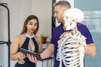 Physiotherapist explains musculoskeletal anatomy using a skeleton model while female patient holds