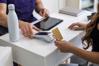 Patient making a contactless payment with a gold credit card on a pos terminal at a medical clinic