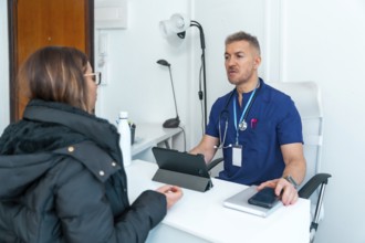 Healthcare professional wearing blue scrubs and a stethoscope talking with a female patient,