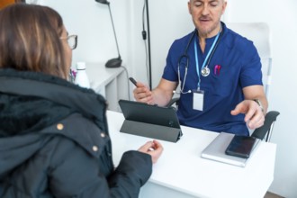 Male doctor wearing scrubs and stethoscope explaining healthcare data to a female patient during a