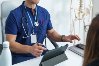 Doctor in scrubs discussing health information with patient, using a tablet for digital records