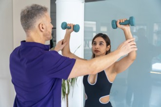 Physiotherapist assisting a young woman with a therapeutic exercise, guiding her arm while she