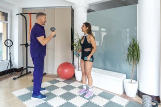 Physiotherapist showing a woman how to perform exercises with dumbbells, focusing on strength