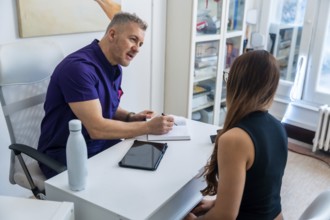 Physiotherapist in purple scrubs discussing treatment plan with a female patient, recording notes