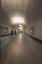 Modern subway tunnel with few passers-by and posters on the walls, London, Great Britain