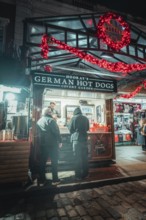 Market stall at night, decorated with Christmas lights, with people in front of it, London, Great