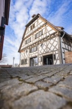 Timbered house with steep roof line against blue sky and cobblestone road, Ötisheim, Enzkreis,