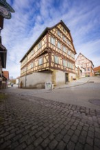 Two large half-timbered houses with red and white details on a busy street corner, Ötisheim,