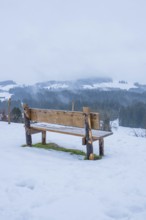 Wooden bench on snowy ground with a view of a quiet winter landscape, Sinnraum, Oberreute, Allgäu,
