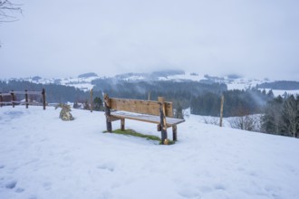 Wooden bench on snow-covered ground with view of winter landscape, Sinnraum, Oberreute, Allgäu,