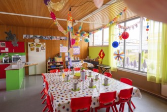 Festively decorated room in kindergarten with long blackboard and colorful chairs, lots of