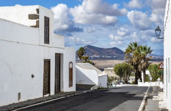 Typical white houses with colored doors and windows in an alley with volcanic craters behind,