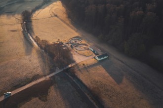 A path leads to a treatment plant with round structures, surrounded by fields and forest at sunset,