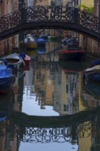 Wrought iron bridge reflected in the canal, Venice, Veneto, Italy