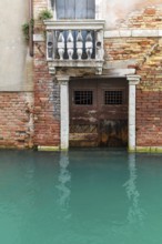 Dilapidated house façade with balcony and door on the canal during floods, Venice, Veneto, Italy