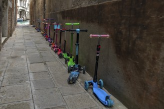 Parked colorful children's scooters, scooters on a wall in front of a kindergarten, Venice, Veneto,