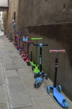 Parked colorful children's scooters, scooters on a wall in front of a kindergarten, Venice, Veneto,