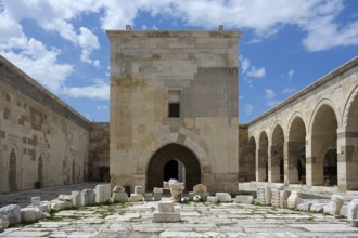 Old courtyard with stone arches and scattered ruins under a clear sky, Sultanhani caravanserai, on