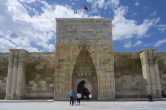Detailed historic gate with stone walls and people in the foreground, richly decorated portal of