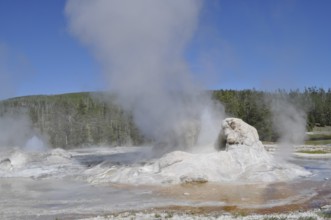 A geyser emits steam surrounded by rocks and natural landscape, Yellowstone National Park, Wyoming,