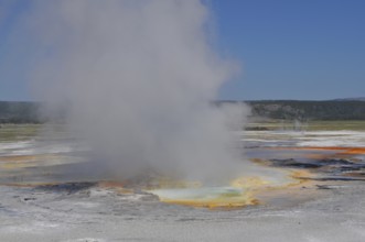 Colorful hot spring with steam under clear skies in a vast natural landscape, Yellowstone National