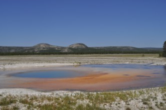 An orange geothermally active area in front of a mountainous landscape, Yellowstone National Park,