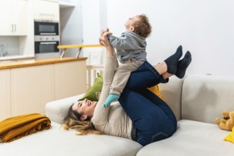 Mother lies on sofa lifting her laughing toddler into the air for a playful airplane ride, sharing