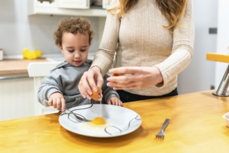 Mother teaching young child to crack an egg and prepare ingredients at the kitchen counter, bonding