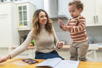 Mother and young child bonding over a coloring book and watercolor palette on a kitchen table,