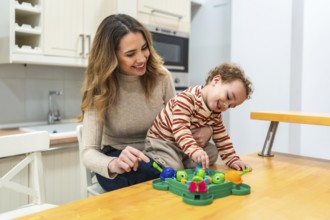 Happy mother and her toddler son enjoying a fun board game together at the kitchen table, sharing