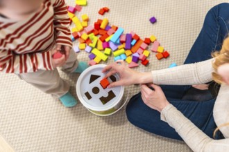 Mom assisting her toddler with a shape sorter toy and colorful blocks on a rug, fostering early