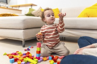 Toddler boy concentrating as he builds a tall wooden block tower on the living room carpet while an