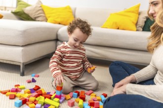 Young child with curly hair is sitting on the floor, deeply engaged in stacking colorful wooden