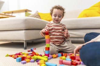 Young boy playing with colorful wooden building blocks, concentrating on constructing a tall tower
