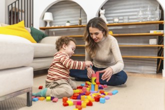Mother and son bonding while happily playing with colorful wooden blocks on the living room floor,