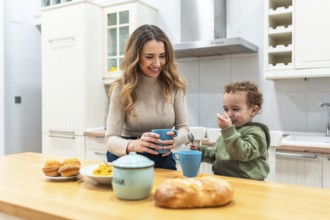 Mother and toddler share a warm morning at the kitchen counter, woman smiling with a mug while the