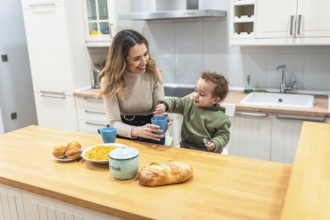 Young mother and toddler son share a cheerful breakfast at the bright kitchen island, bonding over