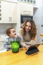Young mother and toddler son share popcorn and smiles while watching a tablet in their modern