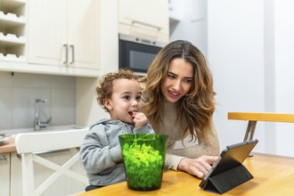 Young mother teaching and entertaining her child with a digital tablet while enjoying a snack