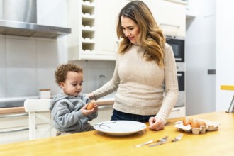Happy mother and curious toddler boy bonding in the kitchen, preparing fresh eggs for a healthy