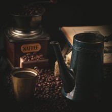 Coffee grinder, antique pot and mug with coffee surrounded by coffee beans and old books