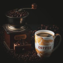 Cup of coffee next to an old coffee grinder full of coffee beans, dark ambiance