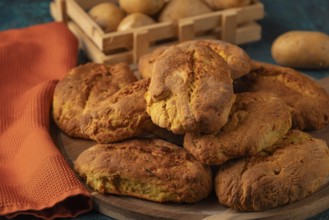 Freshly baked potato rolls with golden brown crust on a wooden board, potatoes in the background