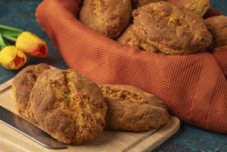 Fresh potato rolls in a basket with orange cloth, some on a wooden board