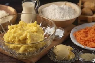 Mashed potatoes and grated carrots next to flour and milk on a wooden table