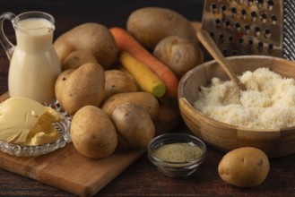 Different ingredients such as potatoes, carrots, parmesan and milk on a kitchen table