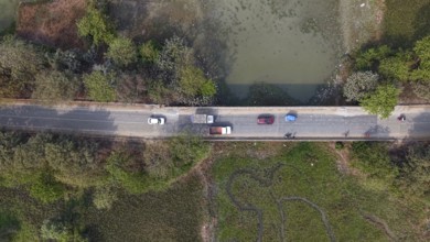 Aerial top-down view of vehicles traveling along a rural road bordered by wetlands and dense